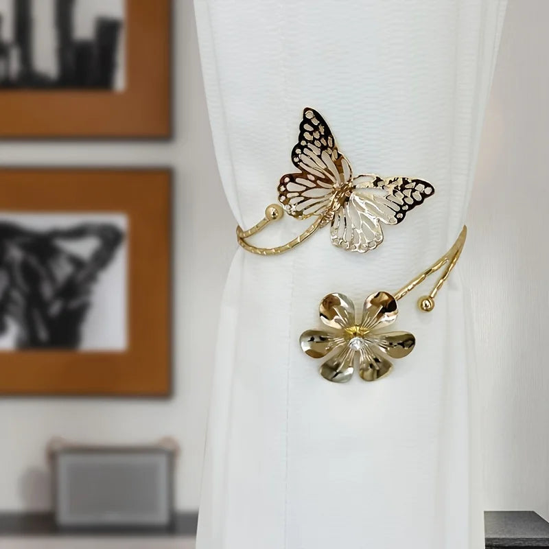 A set of two decorative gold and black butterfly and flower curtain tiebacks hanging from a white fabric.