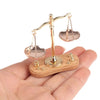 A vintage miniature balance scale with gold-toned arms and plates rests on a wooden base, held in a person's hand.