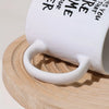 A white ceramic coffee mug with a handle rests on a light wooden cutting board.
