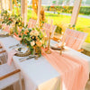 A long white table set for a wedding featuring peach colored fabric draping and floral arrangements.