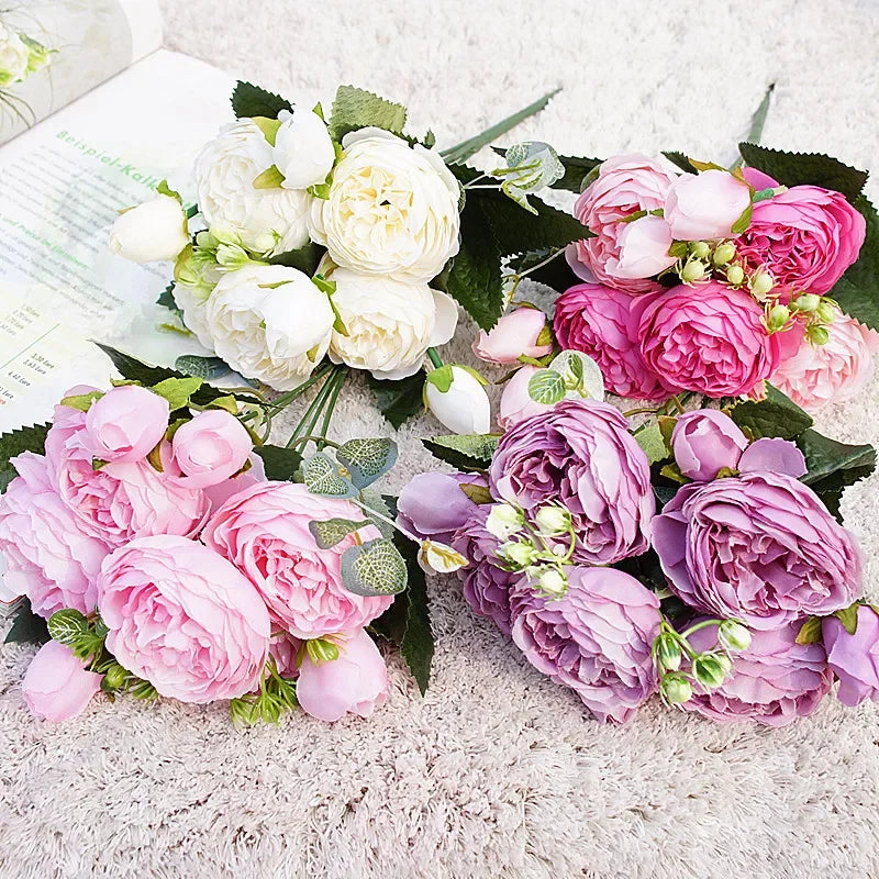 A lush artificial bouquet featuring pink and white roses and peonies on a light background.