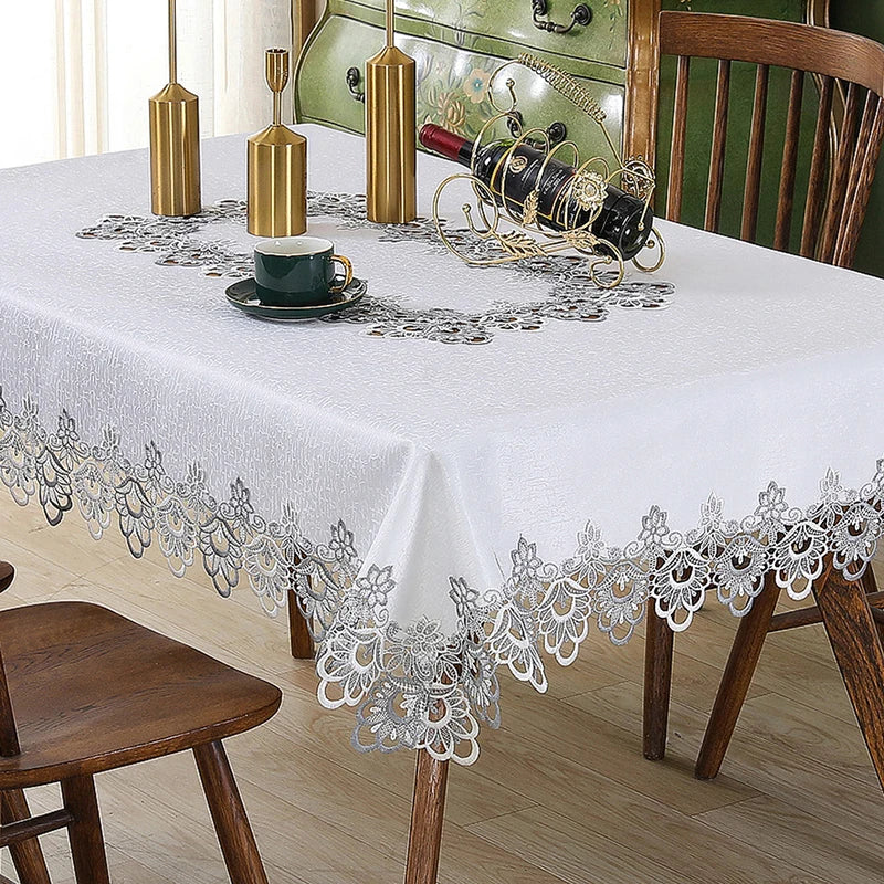 White tablecloth with silver lace trim set for a meal featuring a green cup and wine bottle.