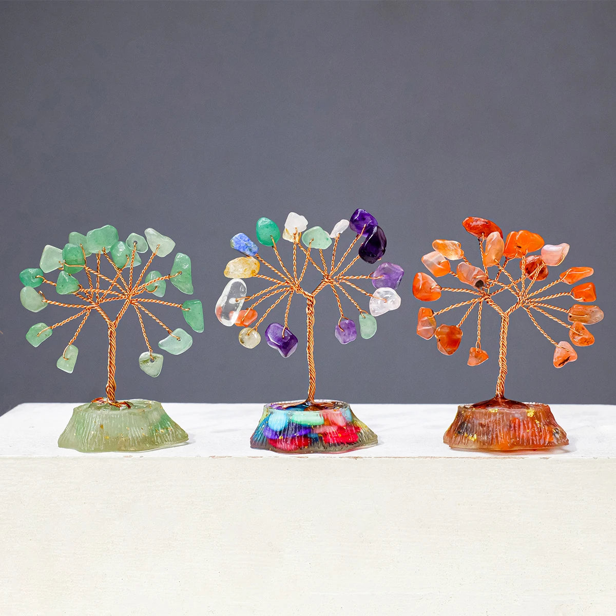 Three crystal trees display various natural colored stones on wooden stands.