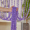A hand is pulling a purple beaded string curtain with tassels, showcasing the bohemian drape texture.