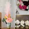 A floral arrangement featuring pink peonies and greenery in a pale green vase, next to decorative pearl string beads.