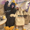 Two people wearing cozy hooded lounge robes, one dark gray and one cream, posing indoors.