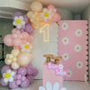 A balloon decoration featuring pink, purple, and white balloons arranged in a vertical garland against a light pink backgroun