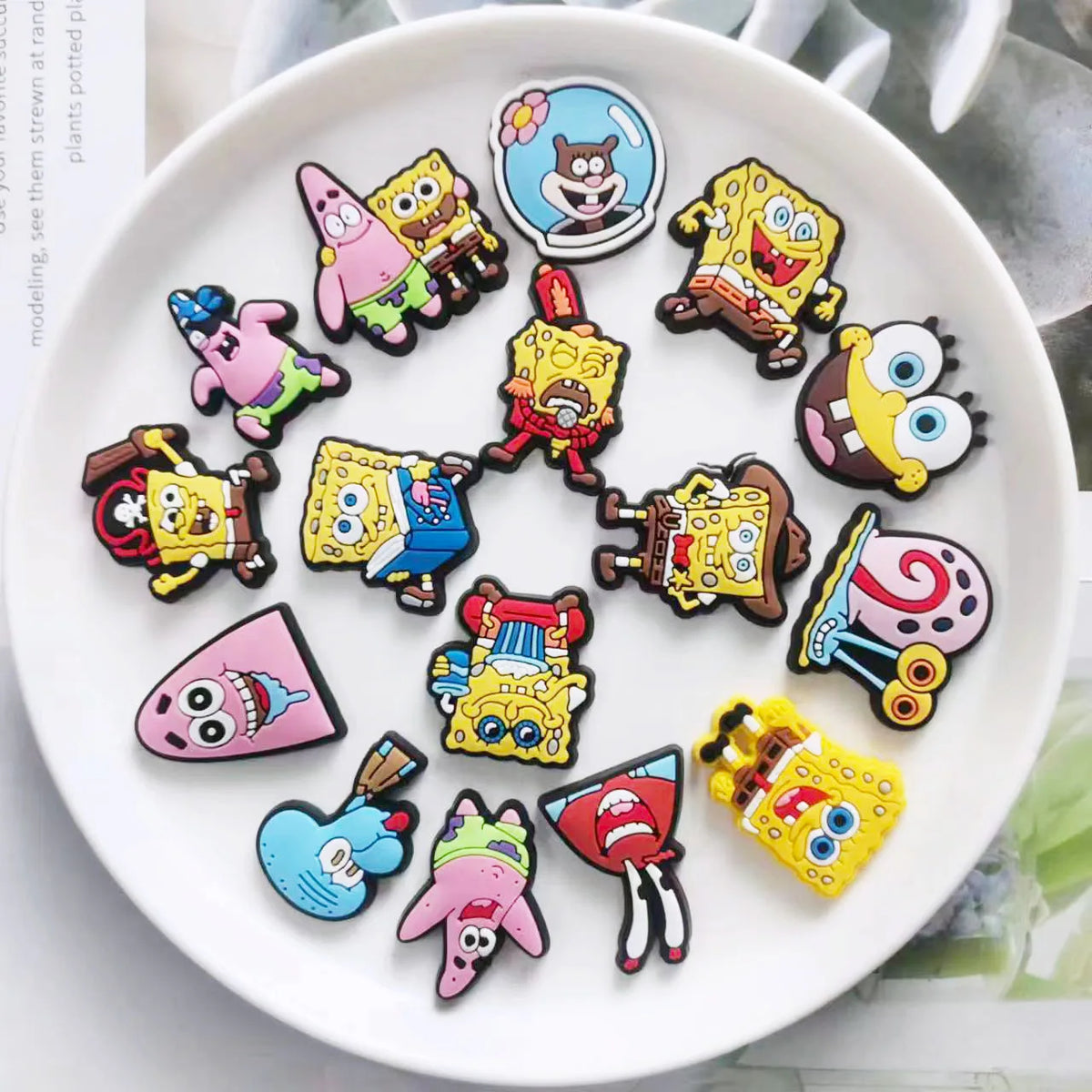 A collection of colorful SpongeBob SquarePants themed shoe charms and pins arranged on a white plate.
