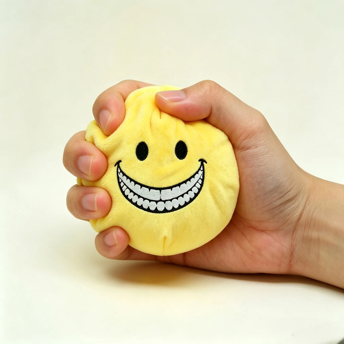 A hand is holding a yellow plush doll shaped like a smiling face with a wide toothy grin.