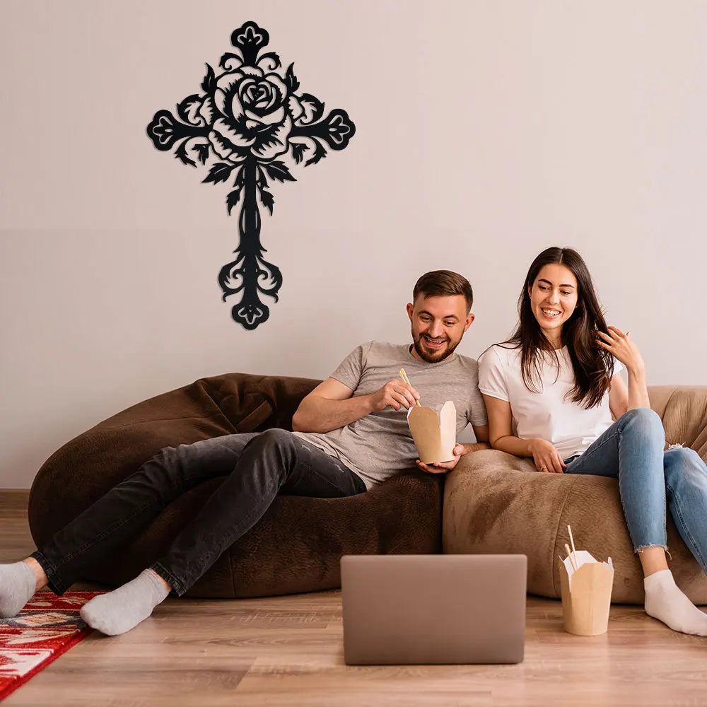 A woman and a man relax on a couch while holding coffee cups in front of an elegant metal cross wall decor.
