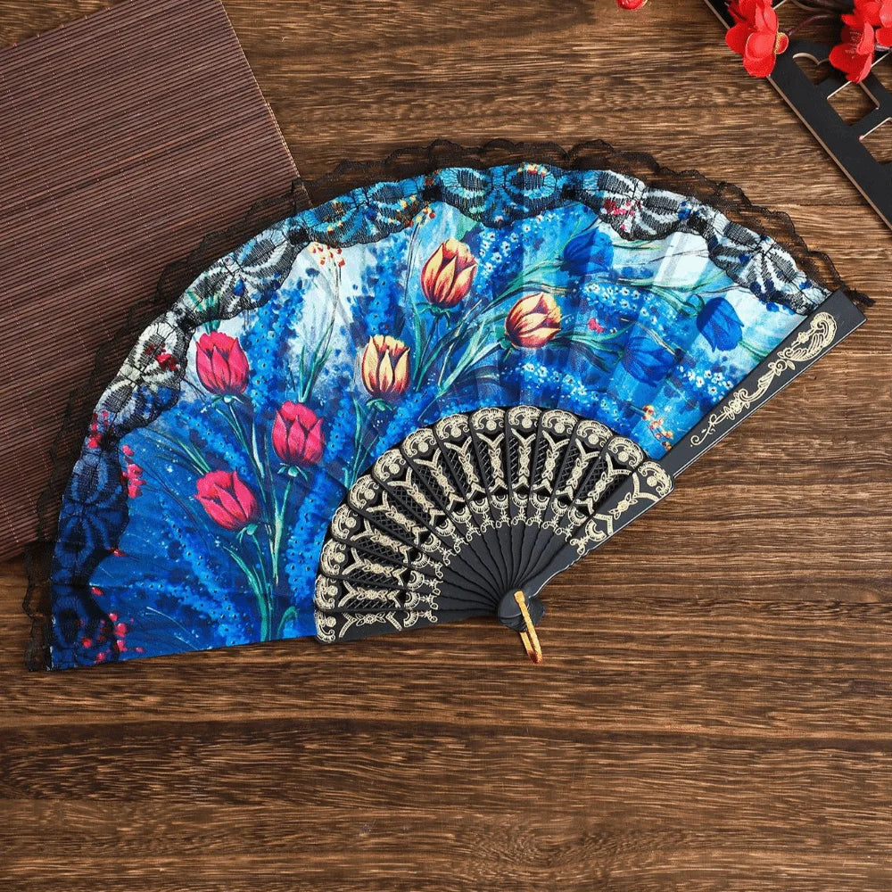 A blue and white floral Spanish style folding lace trim handheld fan resting on a wooden surface.