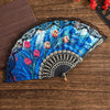 A blue and white floral Spanish style folding lace trim handheld fan resting on a wooden surface.