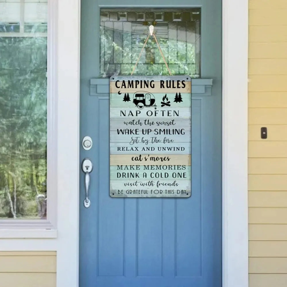 A vertical weathered wooden sign with white text listing camping rules like nap often, watch the sunset, and relax and unwind