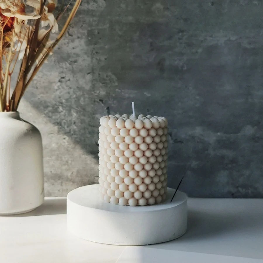 A white Nordic bubble scented soy candle sits on a round white pedestal against a gray textured wall.