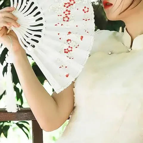 A woman holds an elegant white folding fan decorated with red plum blossoms.