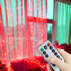 A hand holds a remote control for LED curtain fairy lights illuminating bright pink sheer curtains.