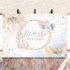 A watercolor-style gender reveal backdrop featuring floral elements and gold accents for a baby announcement.