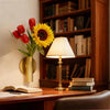 A minimalist wall-mounted metal flower vase holding red tulips and a yellow sunflower on a wooden desk.