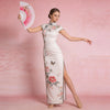 A woman models a white floral print dress and a pink folding fan against a pink background.