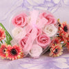 A clear plastic container holds a bouquet of handcrafted soap roses in shades of pink and white.