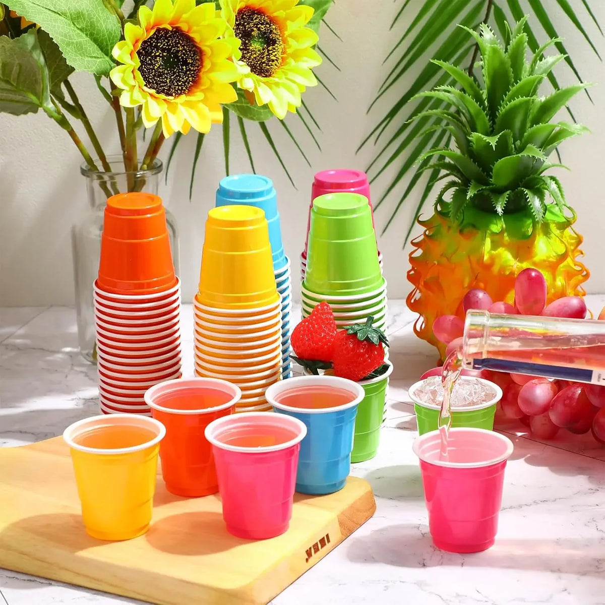A collection of colorful disposable plastic shot cups in various shades of orange, yellow, pink, and blue are arranged on a w