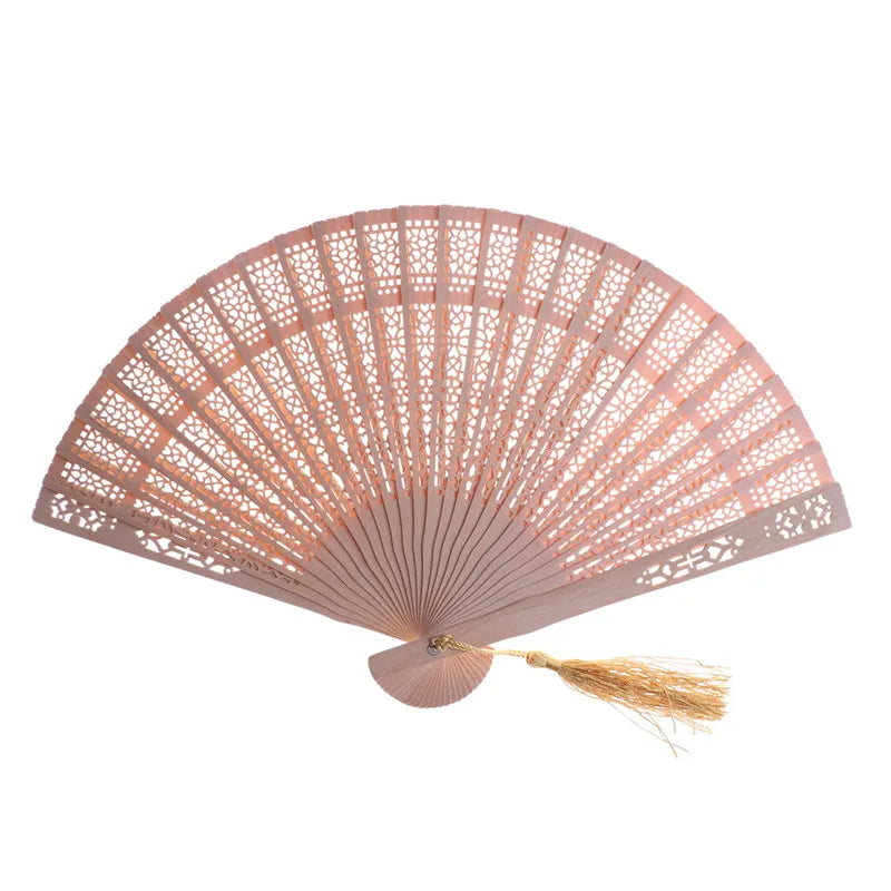 A hand carved bamboo folding fan with a light pink color and natural straw tassel.
