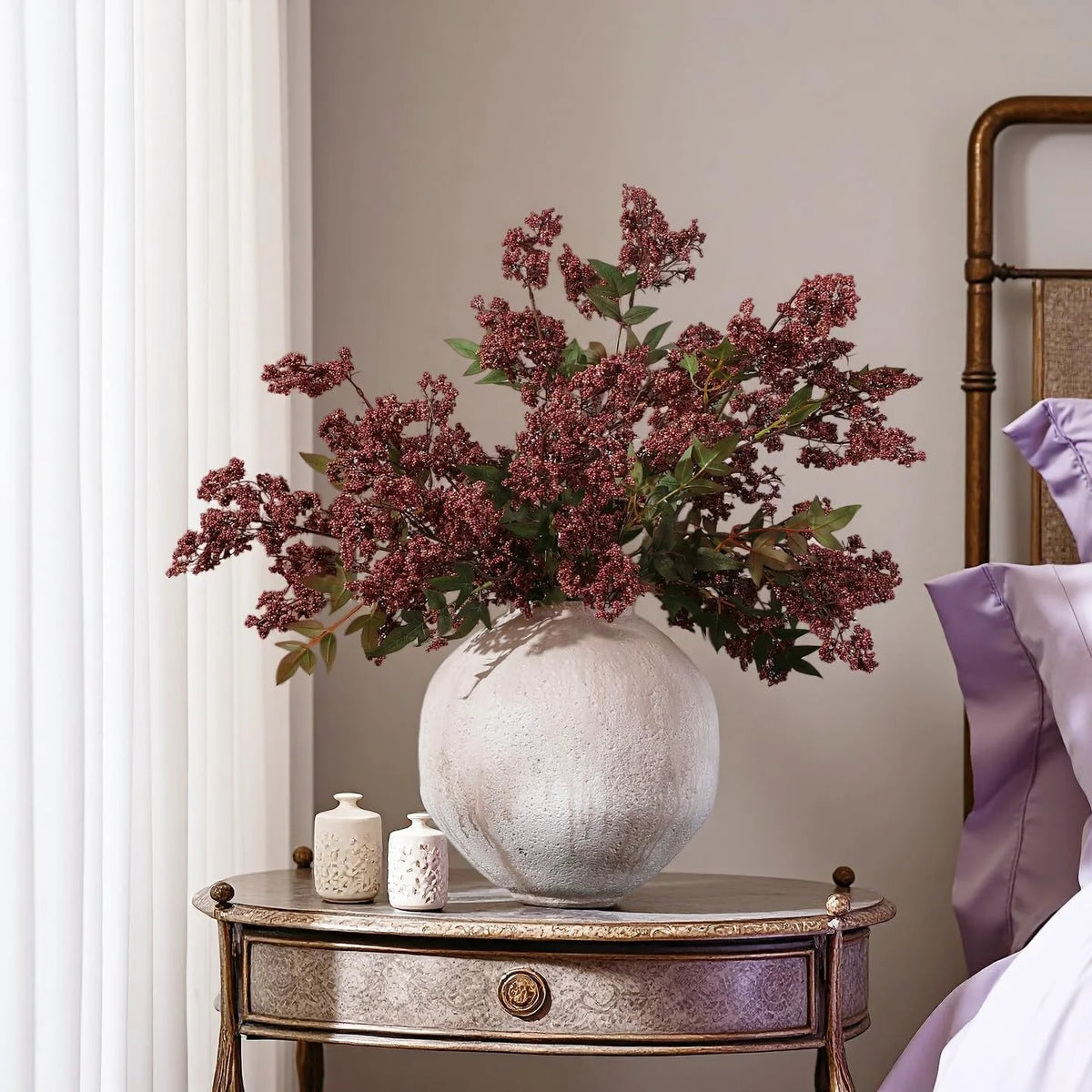 A faux branch of dusty plum nandina berries in a light gray vase on a wooden table.