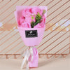 A pink paper bouquet of roses with green leaves tied with a white ribbon.