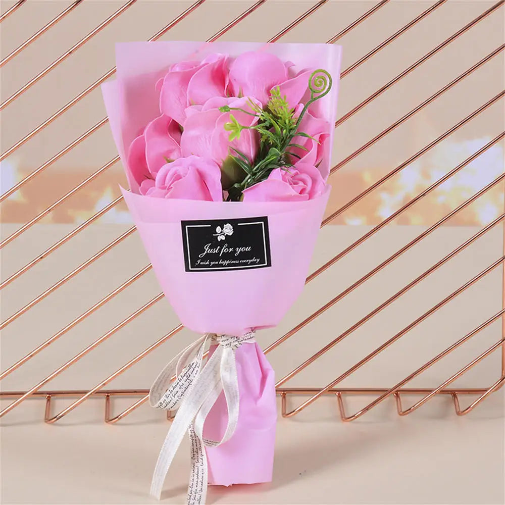 A pink paper bouquet of roses with green leaves tied with a white ribbon.