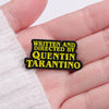 Black enamel pin with yellow text that reads Written and Directed by Quentin Tarantino
