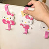 A hand is hanging a pink and white cartoon cat hook onto a white door with a pink hanger.