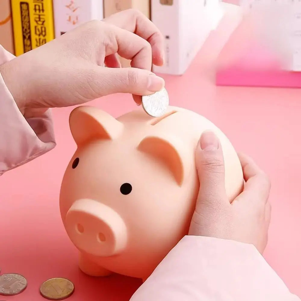A hand is placing a coin into the mouth of an orange piggy bank shaped like a pig.
