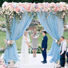 A wedding ceremony setup featuring light blue chiffon drapes and floral arrangements for an outdoor event.