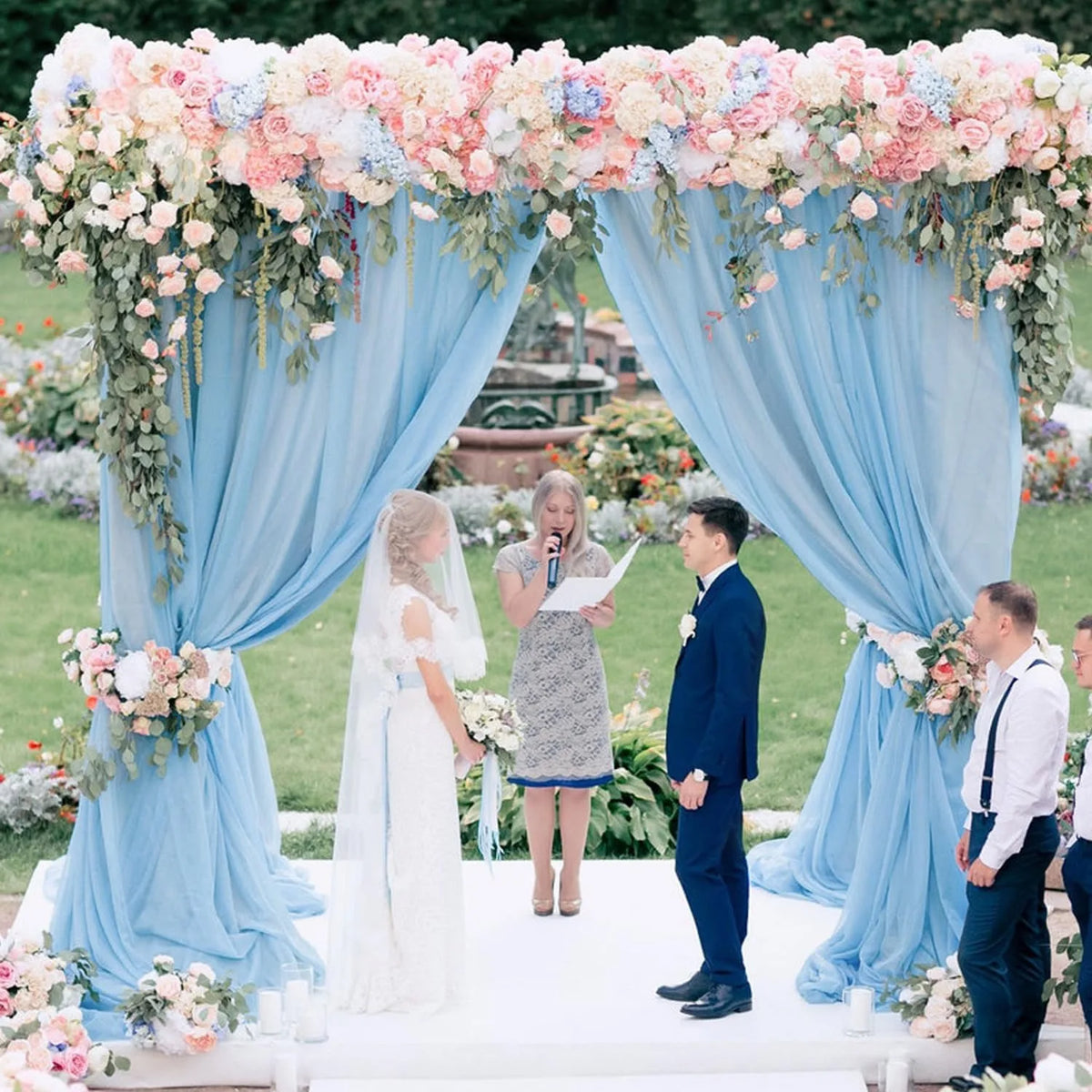 A wedding ceremony setup featuring light blue chiffon drapes and floral arrangements for an outdoor event.