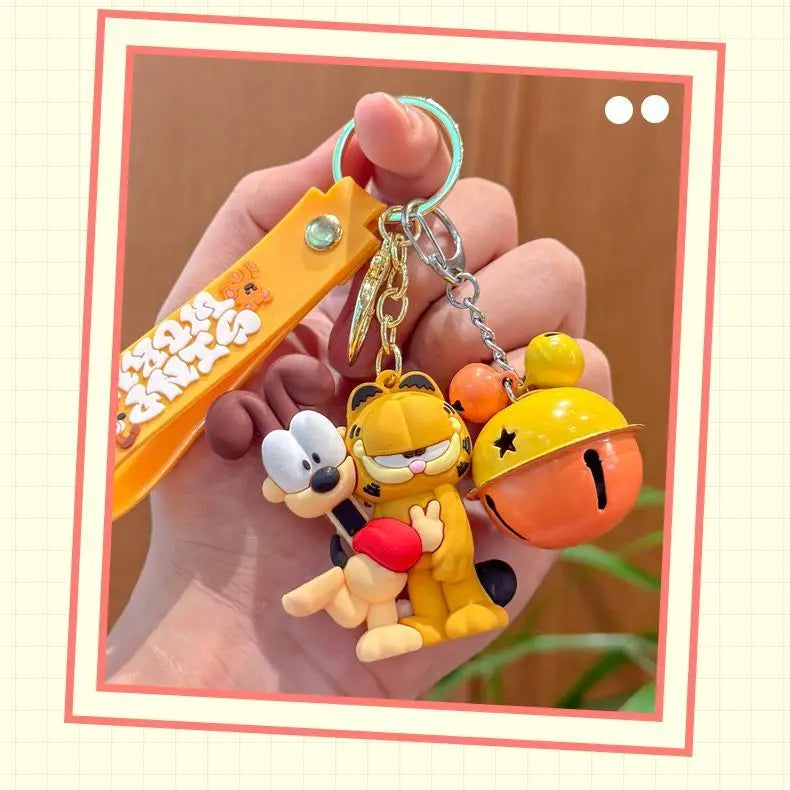 A hand holds a yellow and orange cartoon keychain pendant featuring the characters of Garfield