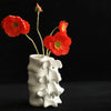 A white ceramic vase shaped like vertebrae holds a single red flower and a green stem.