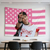 A photo of Hyunjin holding a pink American flag tapestry with a peace sign.