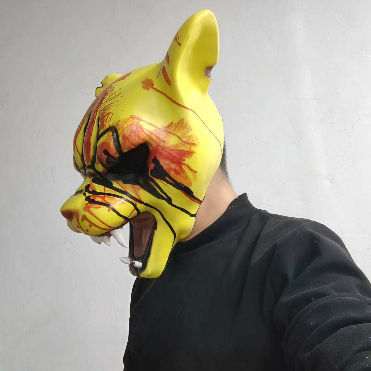 A yellow latex mask shaped like a tiger's head with blood splatter details, worn by a person.