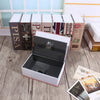 A black lock box with a clear glass window is displayed in an open wooden box surrounded by books.