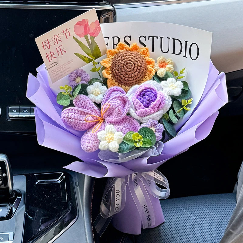 A bouquet of handmade crochet flowers in shades of purple, orange, and white is displayed in a purple paper wrapping.
