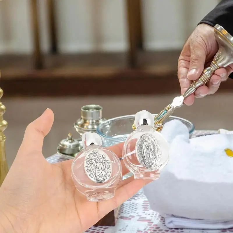 A hand holds a decorative glass bottle with a silver figurine and twist cap on a table.
