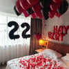 A bed decorated with red confetti and strings of balloons spelling out 22 in black and red colors.