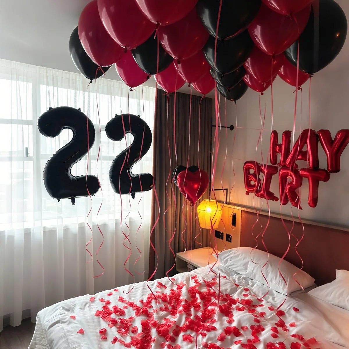 A bed decorated with red confetti and strings of balloons spelling out 22 in black and red colors.