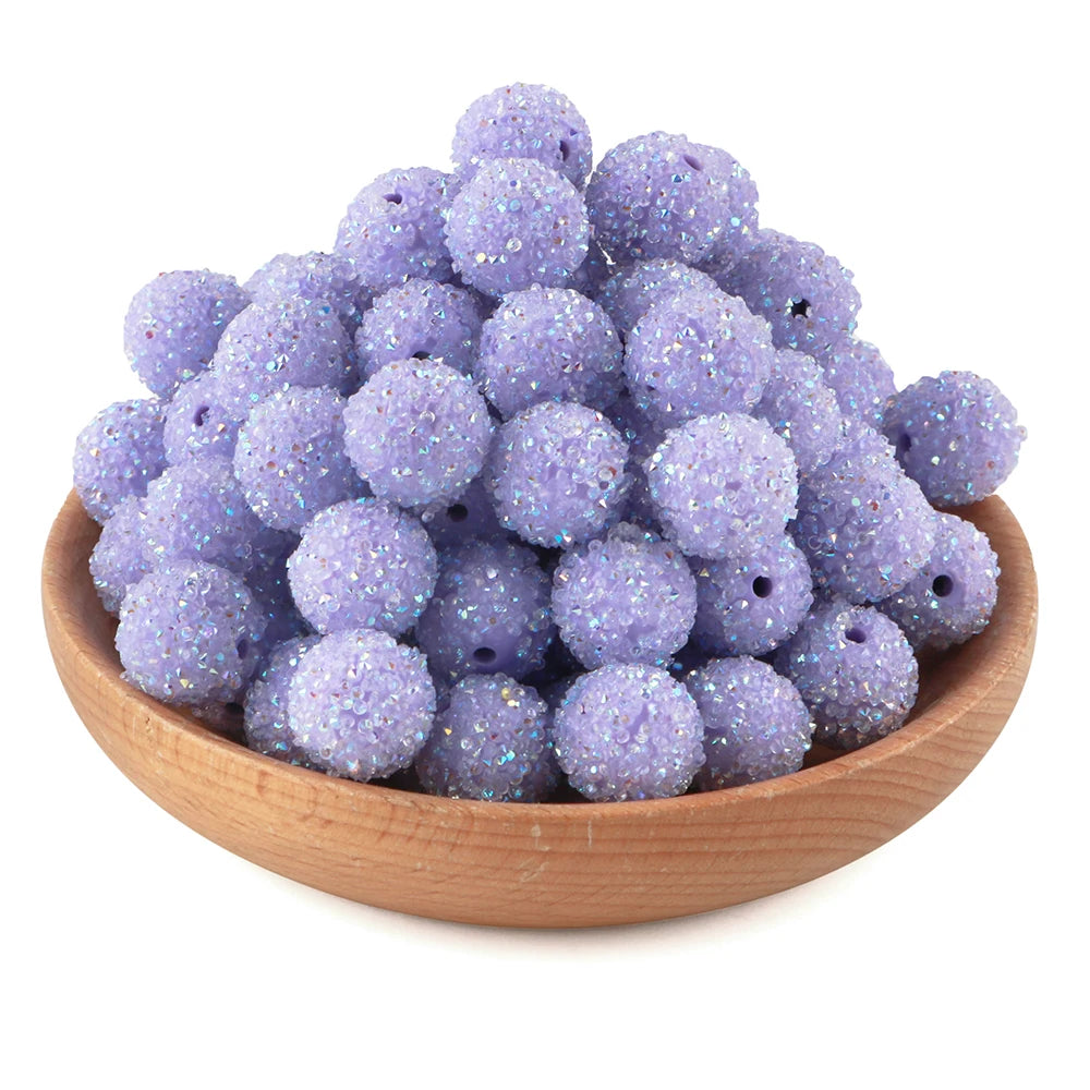 A pile of purple glitter resin beads for jewelry making in a wooden bowl.