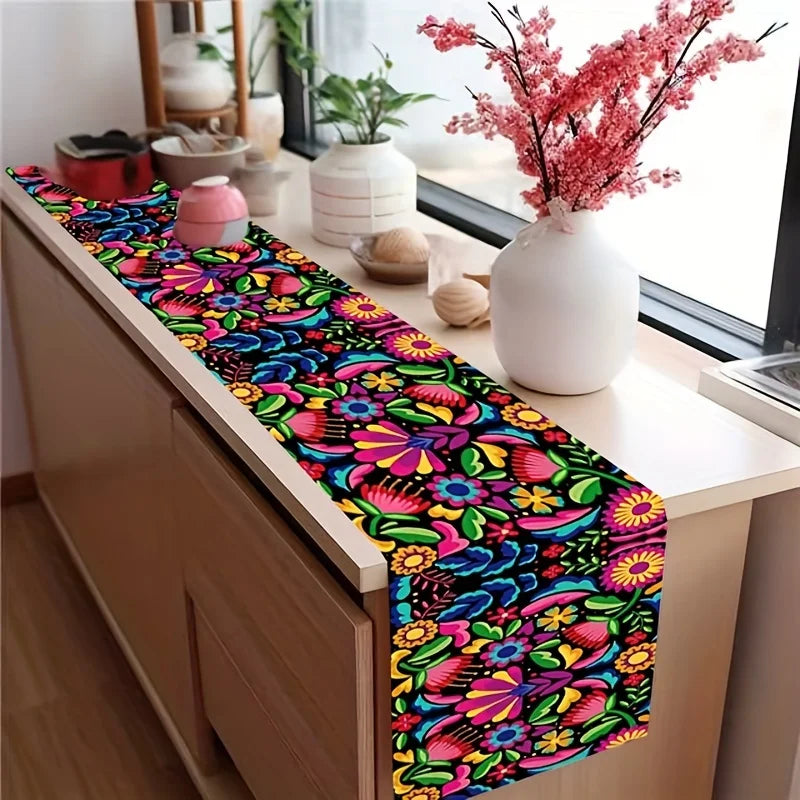 A vibrant floral print linen table runner with pink and purple flowers displayed on a wooden cabinet.