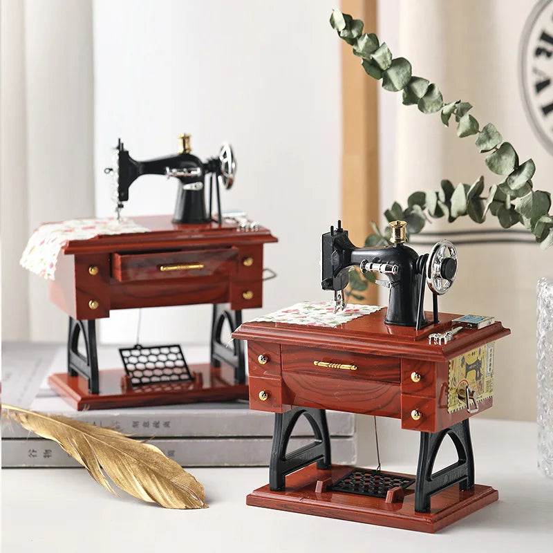 A vintage sewing machine music box with a wooden base and decorative elements sits next to a leafy branch.