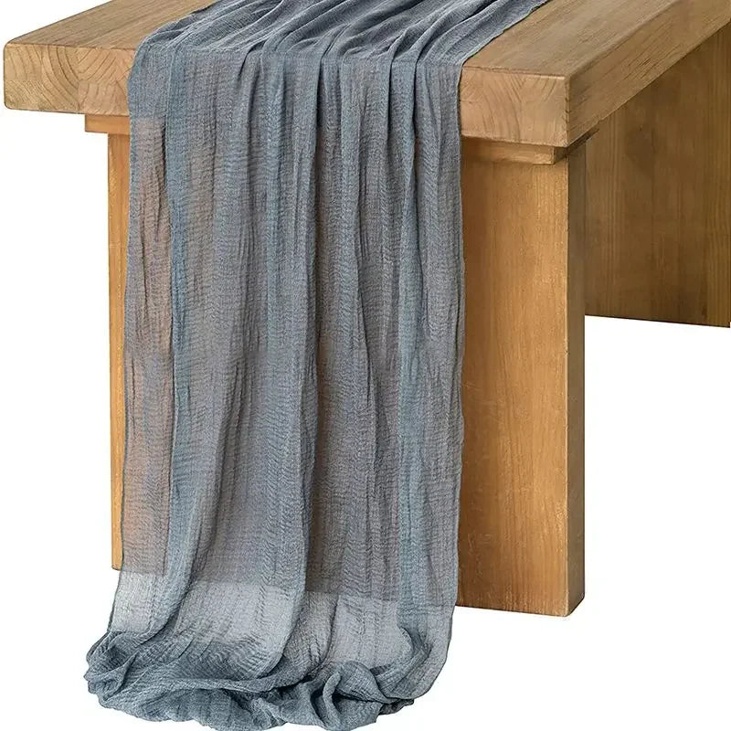 A flowing sage green gauze table runner draped over a wooden table.