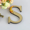 A 3D golden letter S cutout for a mirror wall decal set, placed next to some flowers.