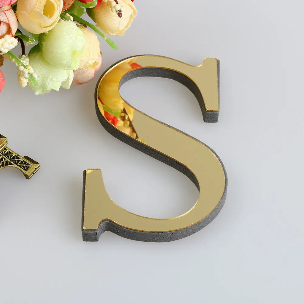 A 3D golden letter S cutout for a mirror wall decal set, placed next to some flowers.