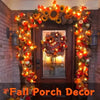 A wooden door decorated with autumn foliage and warm orange string lights for fall porch decor